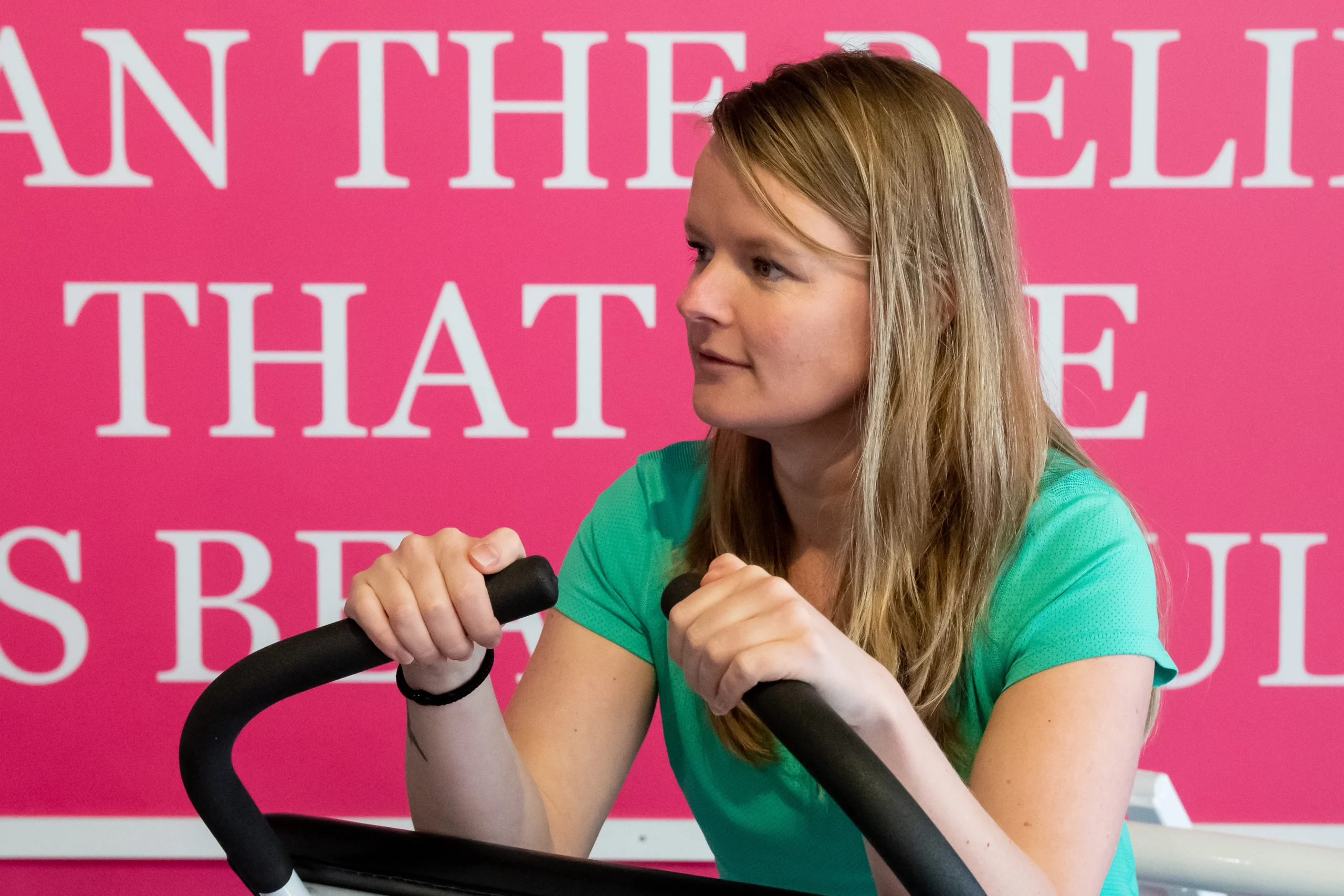 Vrouw met focus die voor de roze muur met slogan staat van StrongHer fitness Hardinxveld