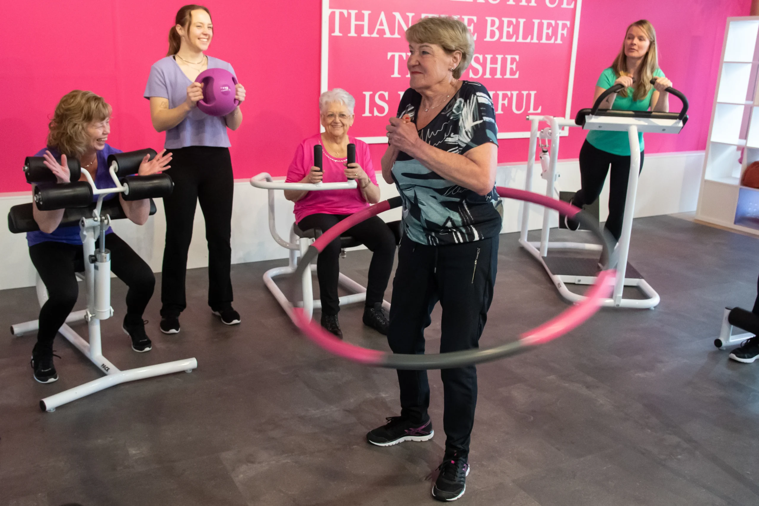 Vrouwen in groepsverband die op fitness toestellen oefeningen doen kijkend naar een vrouw die gebruik maakt van hoolahoop in fitness Hardinxveld